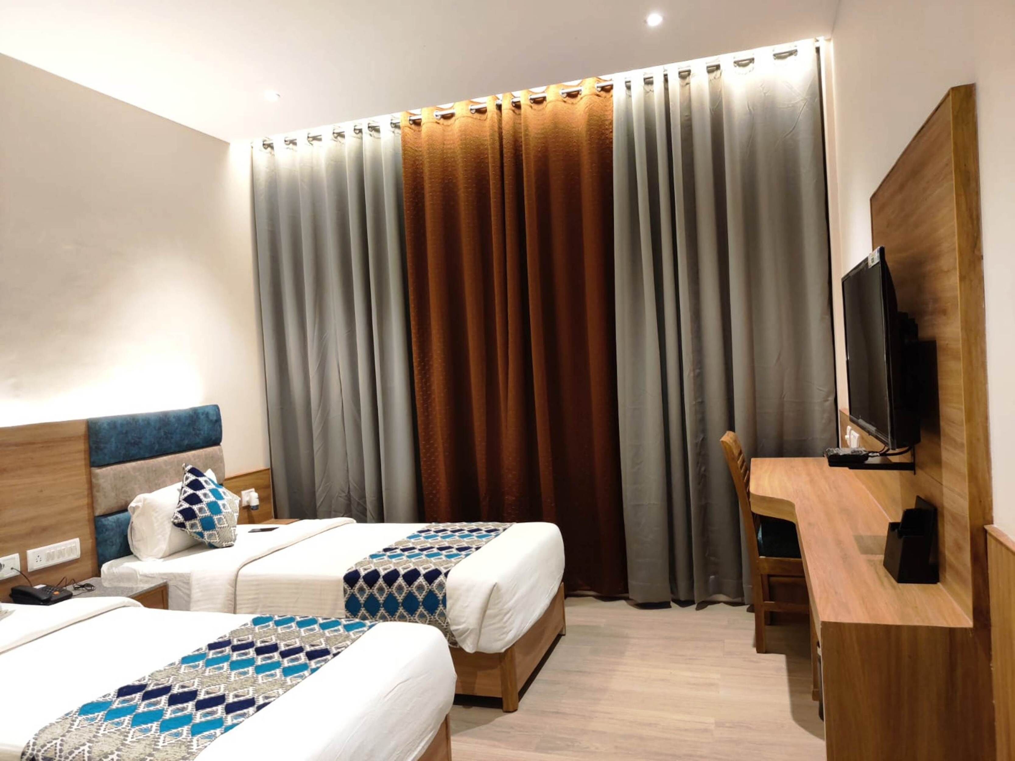Habitación de hotel con dos camas, un escritorio, un televisor y un ventanal con cortinas.