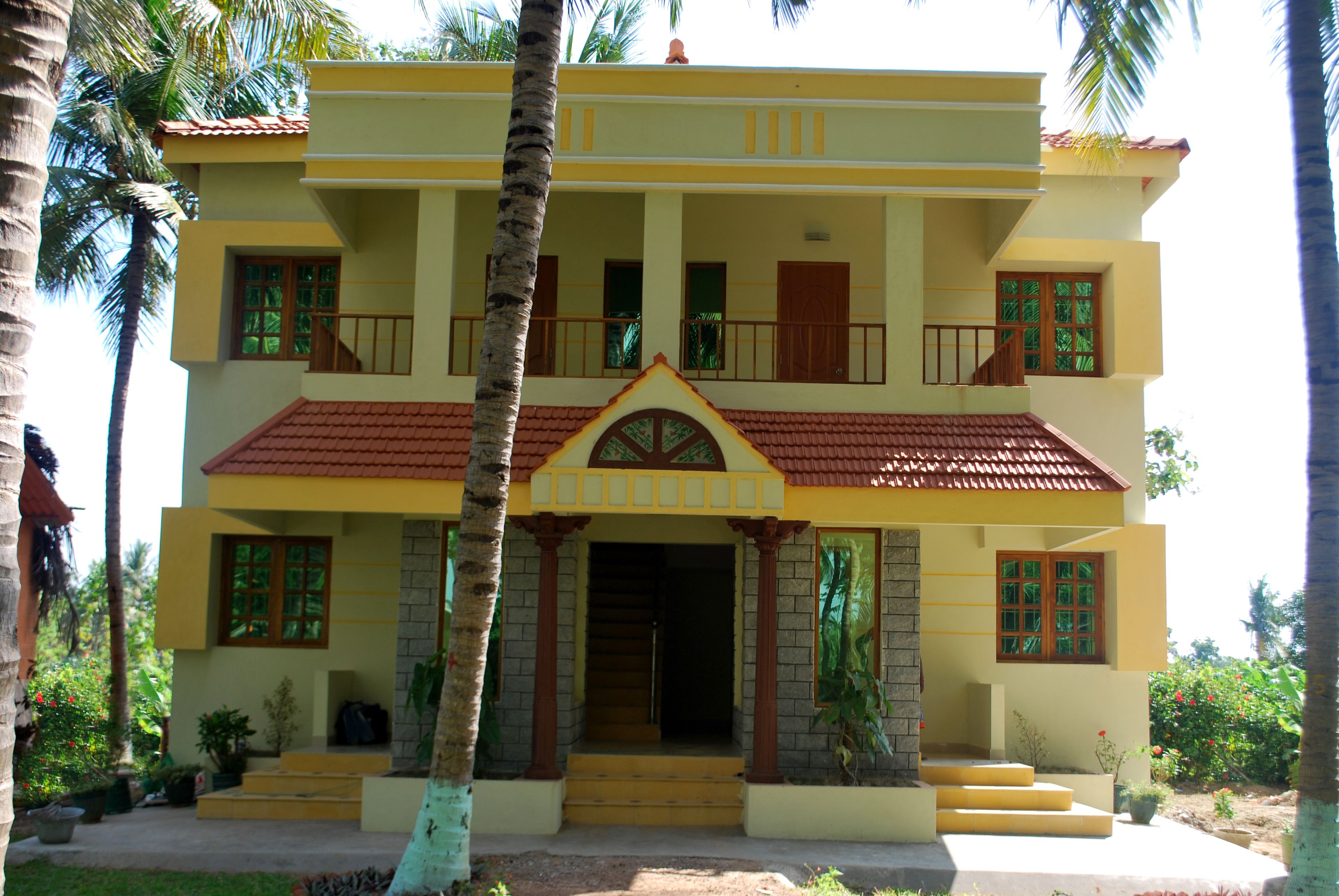 A two-story building with a red-tiled roof, a central entrance with steps, and multiple windows with wooden shutters.