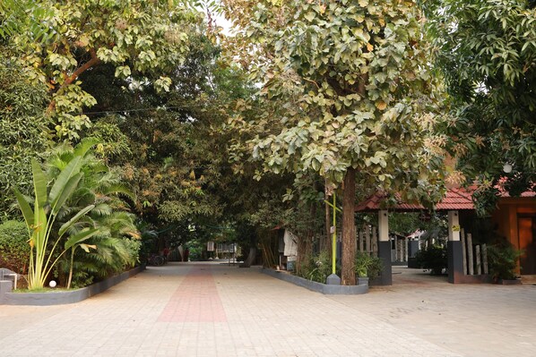 A paved walkway flanked by lush greenery and a covered structure with a red roof.