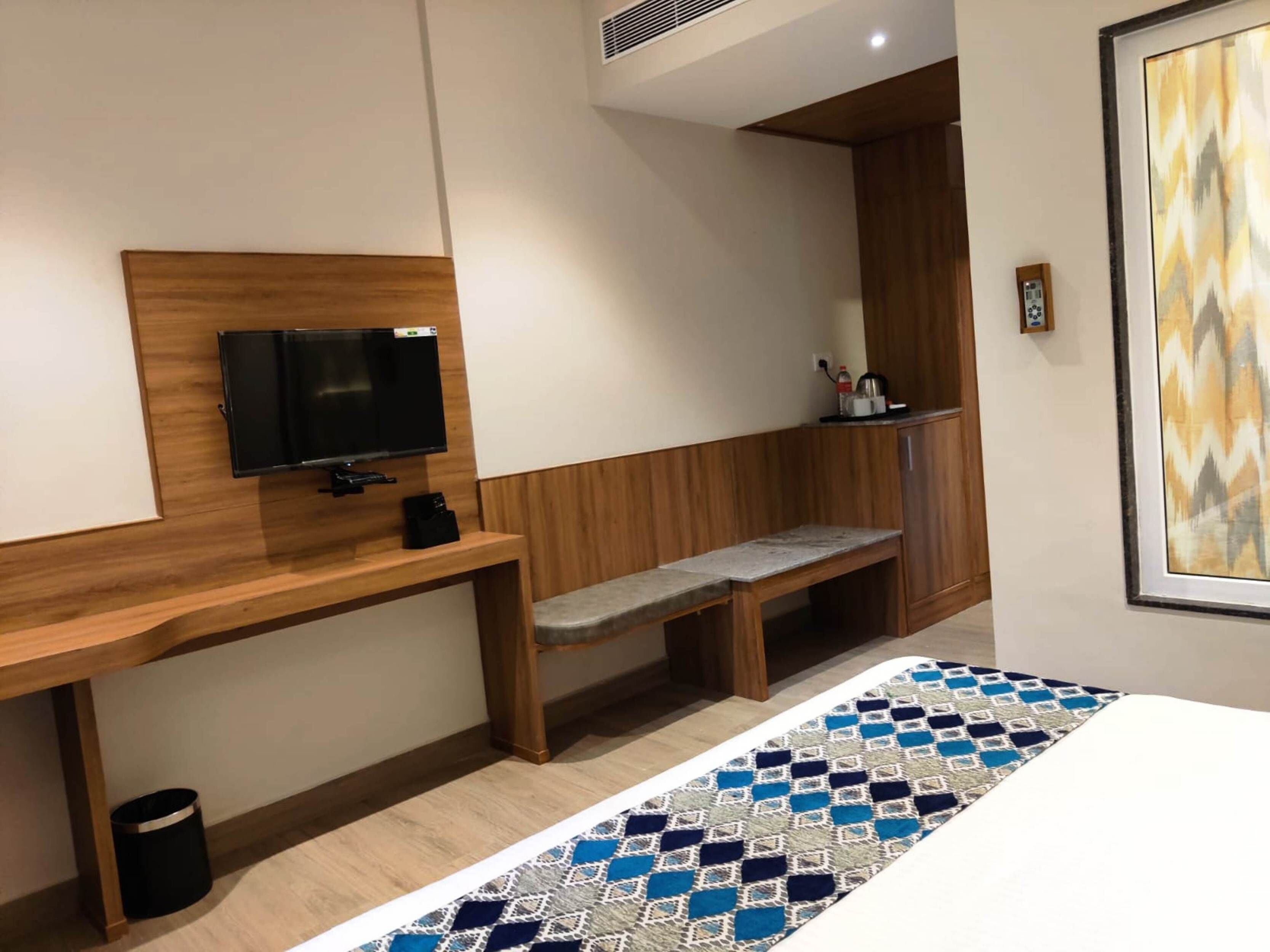 Una habitación de hotel con un escritorio de madera, un televisor, un banco y una alfombra estampada.