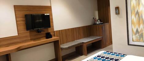 Una habitación de hotel con un escritorio de madera, un televisor, un banco y una alfombra estampada.