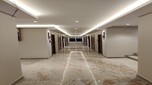 Un largo pasillo bien iluminado, con suelo de mármol y puertas a ambos lados que dan a habitaciones.