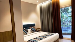 Habitación de hotel moderna con una cama grande, un cabecero de madera y vistas a un balcón con follaje.