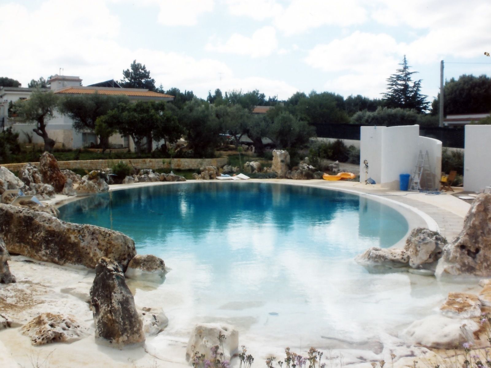 Una piscina de borde curvo, rodeada de rocas y un muro blanco.