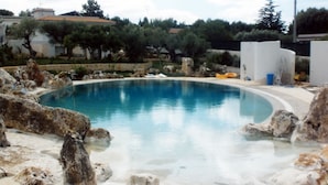 Una piscina de borde curvo, rodeada de rocas y un muro blanco.