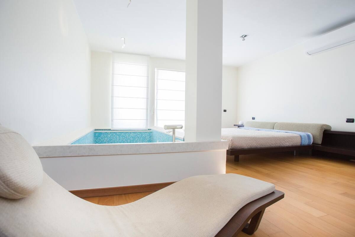 Ein modernes Zimmer mit großem Fenster, kleinem Pool, Bett und Stuhl.