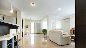 Un salón amplio con una cocina moderna, un comedor con taburetes blancos y una zona de estar cómoda con sofá y mesa de centro.