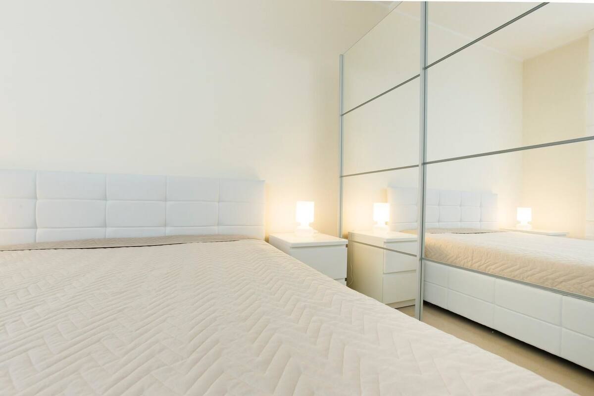Ein modernes Schlafzimmer mit einem großen Bett, Nachttischen und einem raumhohen Spiegelkleiderschrank.