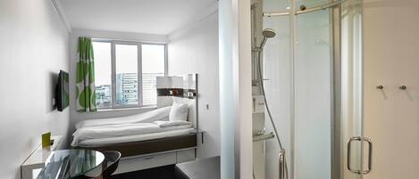 Una habitación de hotel moderna con una cama, un escritorio de vidrio, ducha y vistas a la ciudad.
