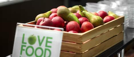 A wooden crate filled with red apples and green pears on a table with a sign that reads "LOVE FOOD hate waste."
