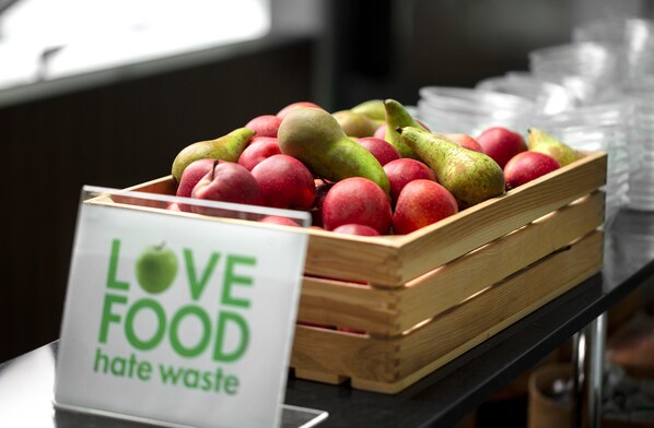 Une caisse en bois remplie de pommes rouges et de poires vertes est posée sur une table, et une pancarte indique : « Aimons la nourriture, détestons le gaspillage. »