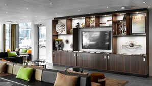En modern hotellobby med en stor TV, bekväma sittplatser och dekorativa föremål utställda på hyllor.
