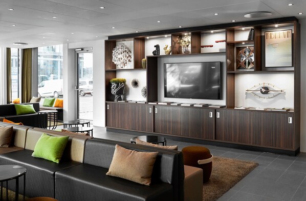 A modern hotel lobby with a large TV, comfortable seating, and decorative items on shelves.