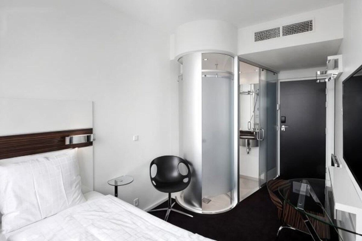 Een hotelkamer met een bed, een glazen douchecabine, een klein tafeltje en een stoel.
