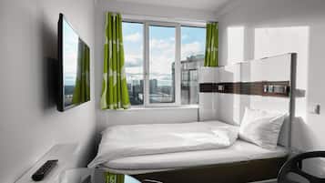 Quarto de hotel com cama, televisão, escrivaninha e janela com cortinas.