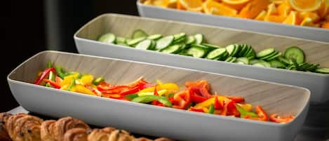 Un bufé con diversas opciones de comida, como verduras cortadas, frutas y pasteles.