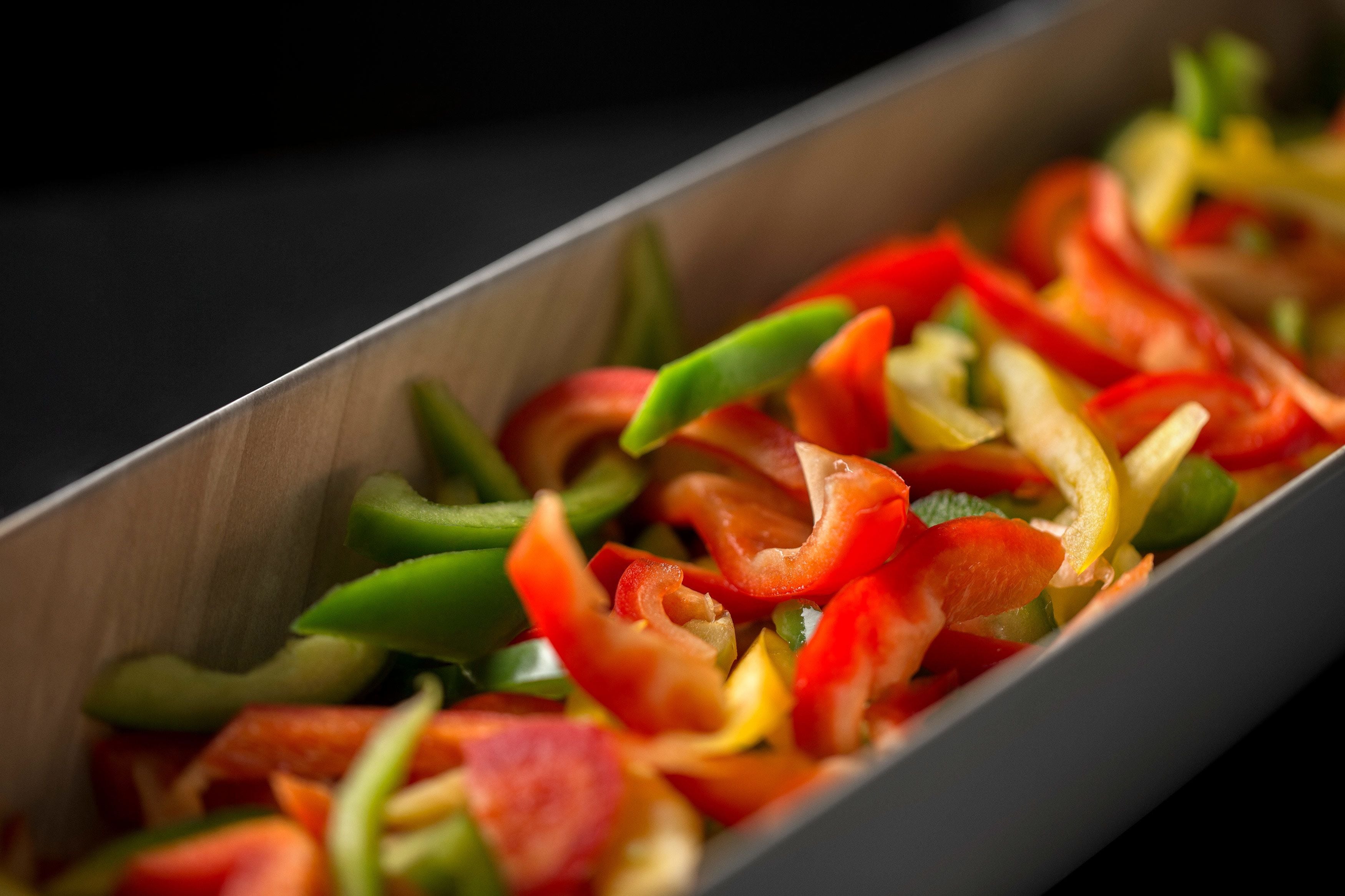 A rectangular metal tray filled with sliced bell peppers in various colors.
