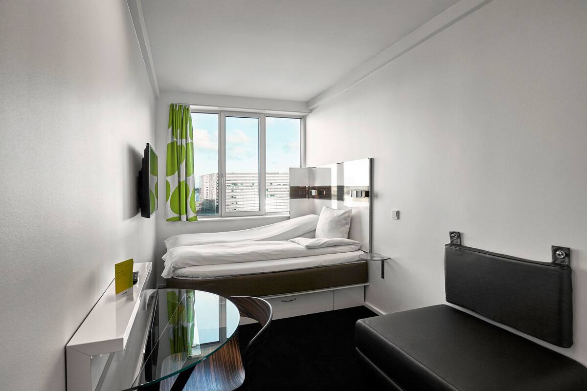 Una habitación de hotel moderna con una cama, un escritorio, una silla y un ventanal grande.