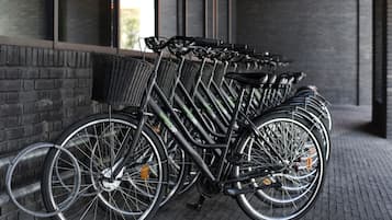 A row of bicycles parked against a brick wall, with a basket attached to one of them.