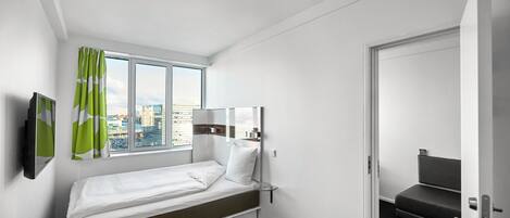 Une chambre d’hôtel avec un lit simple, une fenêtre avec des rideaux, un téléviseur à écran plat et une porte donnant sur un coin salon.