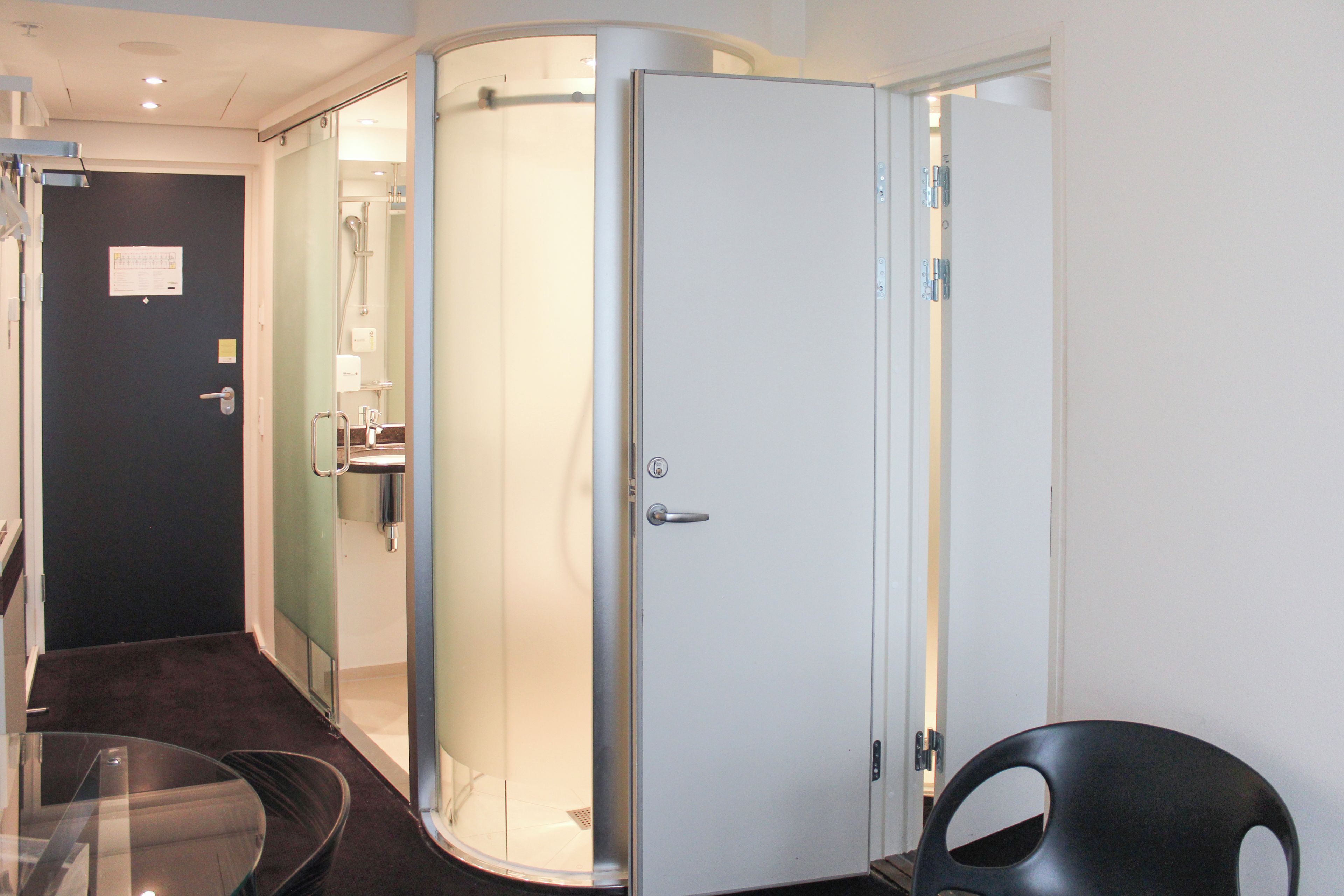A hotel room with a glass partition, a shower area, and a door with a handle.