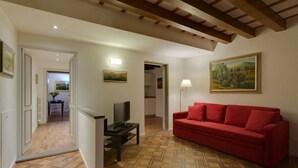 A living room with a red sofa, a television on a stand, and a patterned wooden floor. - A characteristic and comfortable location in the heart of Florence's (Firenze)