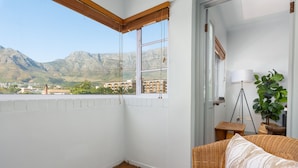 Habitación en esquina con vista a las montañas, una silla de mimbre y una mesita con una lámpara.