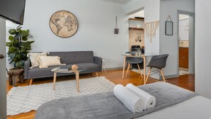 Una sala de estar moderna con un sofá gris, una pequeña mesa de centro y un tapete grande. Se observa un mapa mundial en la pared y una planta a la izquierda.
