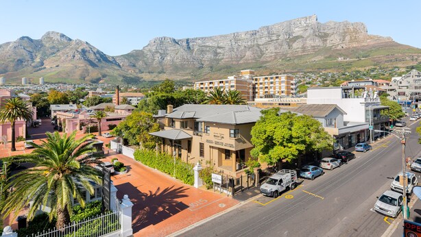 Un hotel con vistas a montañas, una calle con coches y palmeras.
