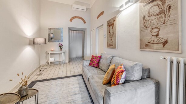 A modern living room with a grey sofa, colorful cushions, a small side table, and a floor lamp. - Apartments Florence - Ghibellina Loft (Firenze)