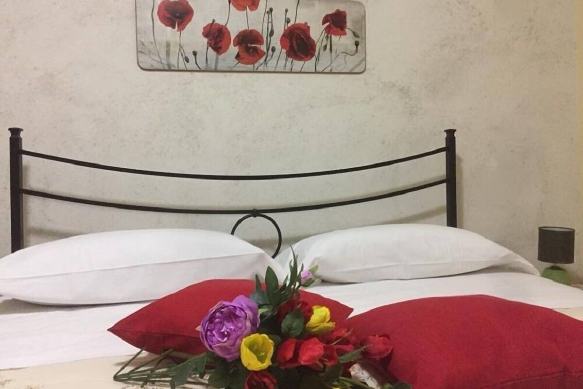 A bed with white bedding, red pillows, and a floral arrangement.