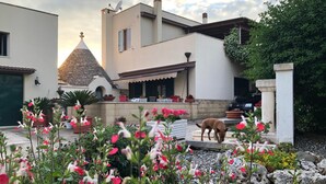 Una casa moderna con techo de tejas, un jardín con flores rosadas y un perro en el patio.