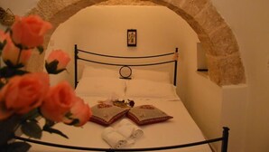 Una cama con un arco de piedra, un cuadro enmarcado encima y una toalla enrollada sobre la cama.