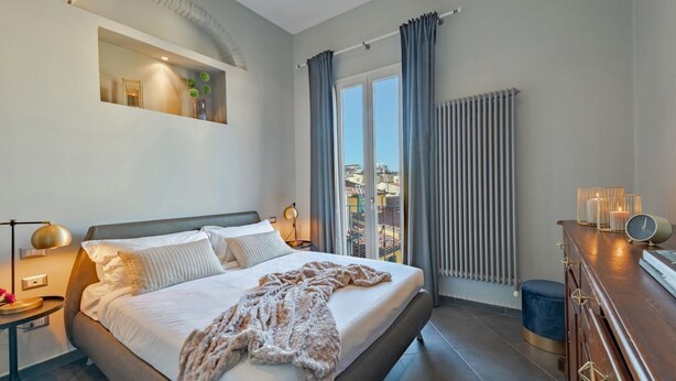 Een moderne slaapkamer met een groot bed, een nachtkastje, een dressoir en uitzicht op de stad door het raam.