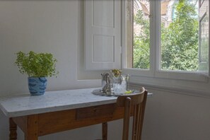 Une cuisine dotée d’un plan de travail en marbre, d’une chaise en bois, d’une plante en pot et d’une fenêtre donnant sur un paysage verdoyant.