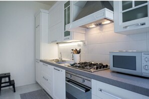 Une cuisine moderne avec des meubles blancs, une cuisinière à gaz, un four à micro-ondes et un petit tabouret.