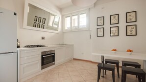 Una cucina moderna con mobili bianchi, piano cottura a gas, forno, lavello e zona pranzo con tavolo bianco e quattro sedie.