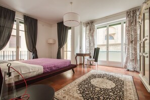 Quarto com cama, escrivaninha, cadeira, luminária e vista para o exterior.
