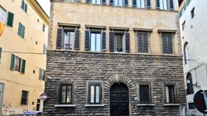 A building with a stone facade, multiple windows with shutters, and a central arched doorway.
