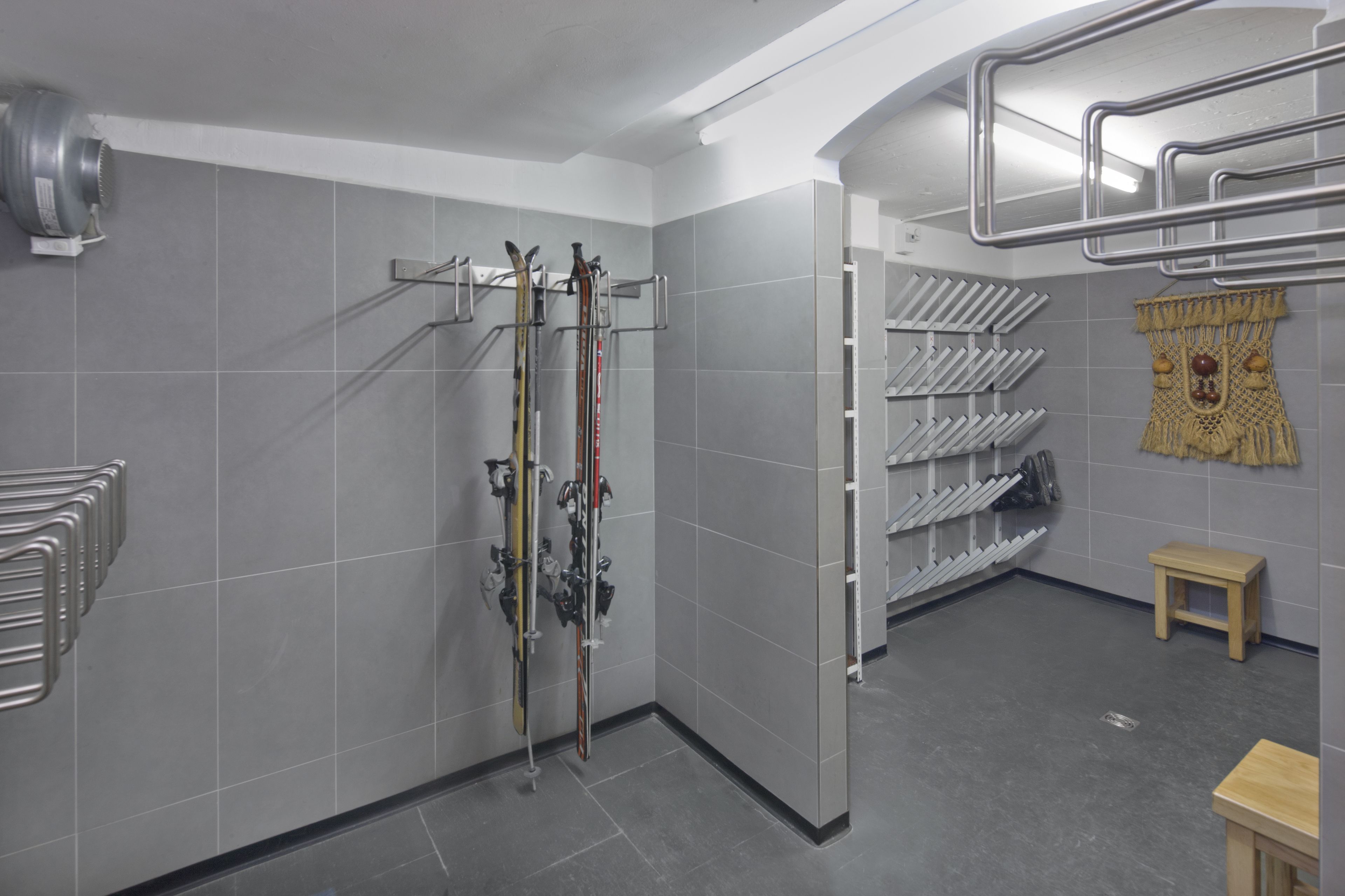 A ski storage room with metal racks for skis and snowboards, a small wooden stool, and a decorative tapestry on the wall.