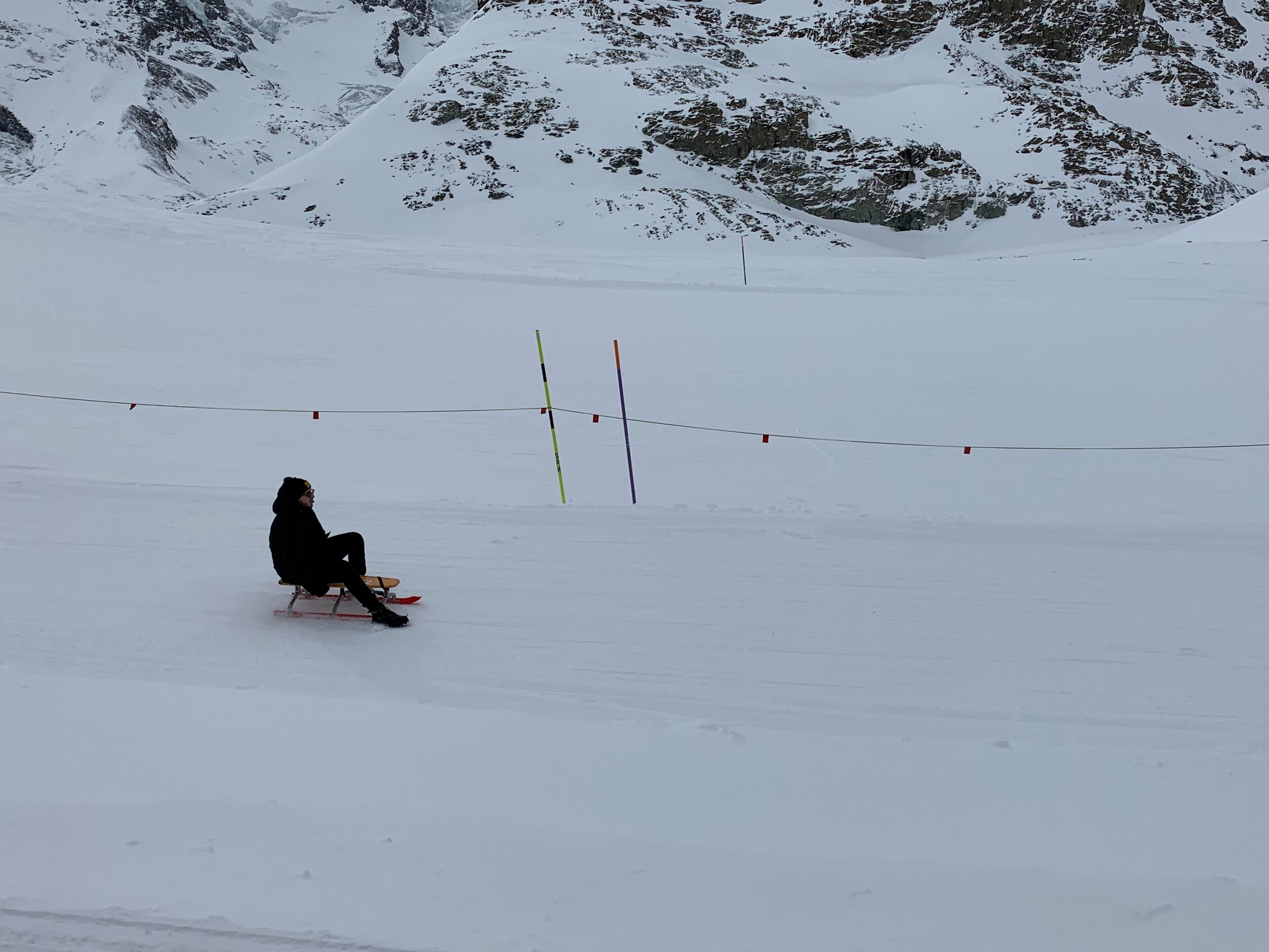A person sitting on a sled in a snowy landscape with mountains in the background.