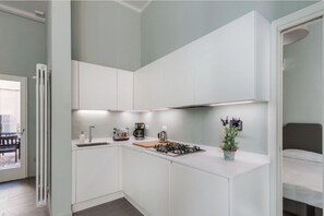A compact kitchen with white cabinets, a gas stove, a coffee maker, and a potted plant.