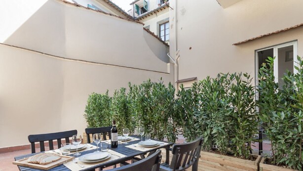 A dining table set outdoors with chairs, plates, glasses, and a bottle of wine. - Apartments Florence - Taddea Terrace (Firenze)