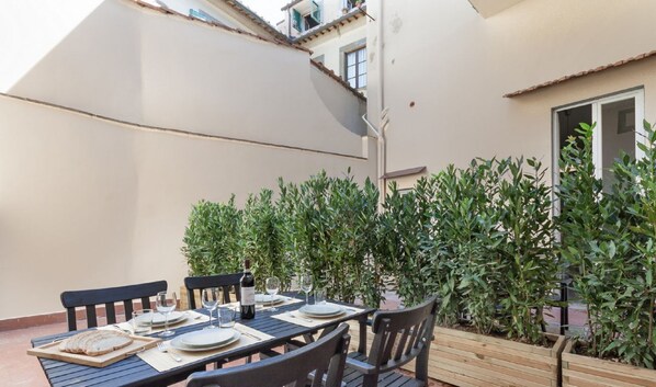 A dining table set outdoors with chairs, plates, glasses, and a bottle of wine.