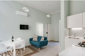 A modern living room with a white dining table, teal sofa, and a flat-screen TV.