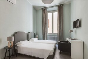 Une chambre d’hôtel avec deux lits, un bureau, une chaise, une télévision et une fenêtre avec des rideaux.