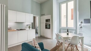 A modern kitchen with white cabinets, a dining area with a white table and chairs, and a large window providing natural light. - Apartments Florence - Taddea Terrace (Firenze)