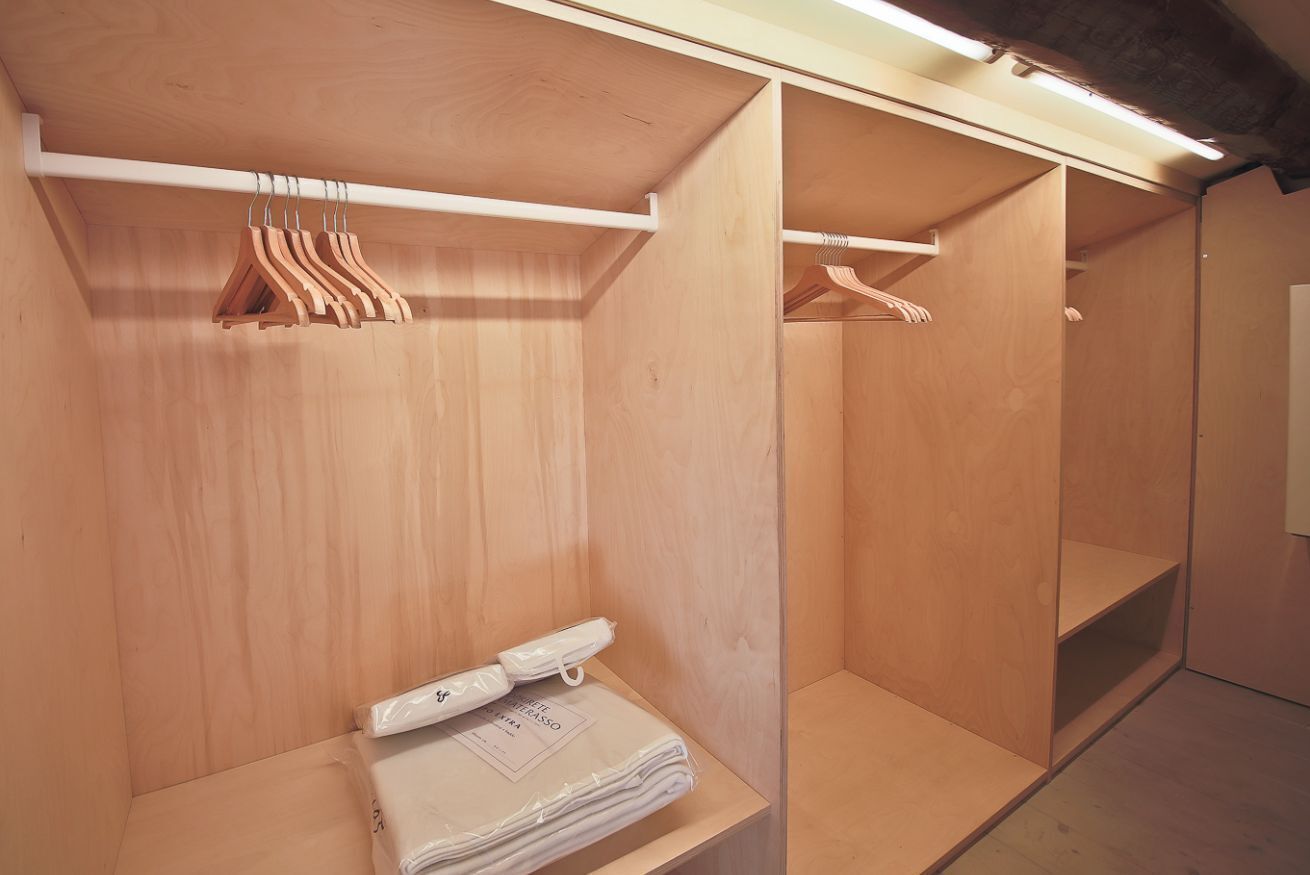A wooden closet with hanging space and a small table with folded items.