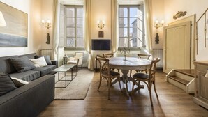 Una habitación con sofá, mesa de comedor, sillas, televisor y una escalera.