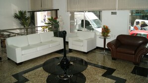 A lobby with a white sofa, a brown leather chair, a black table, and a potted plant. - Itamaraty Hotel (Anapolis)